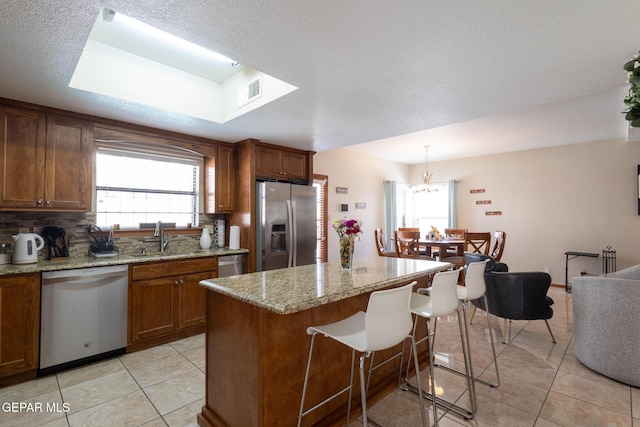 kitchen with brown cabinets, stainless steel appliances, tasteful backsplash, light tile patterned flooring, and a sink