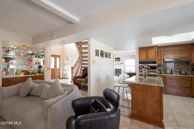 living room with light tile patterned floors, a textured ceiling, visible vents, stairway, and beamed ceiling