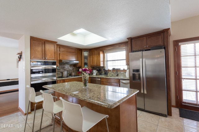 kitchen with appliances with stainless steel finishes, a sink, a wealth of natural light, and under cabinet range hood