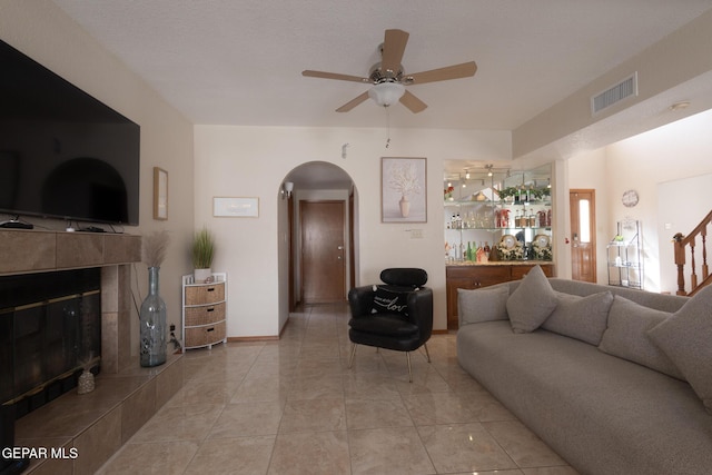 tiled living room featuring visible vents, arched walkways, a tile fireplace, ceiling fan, and stairway