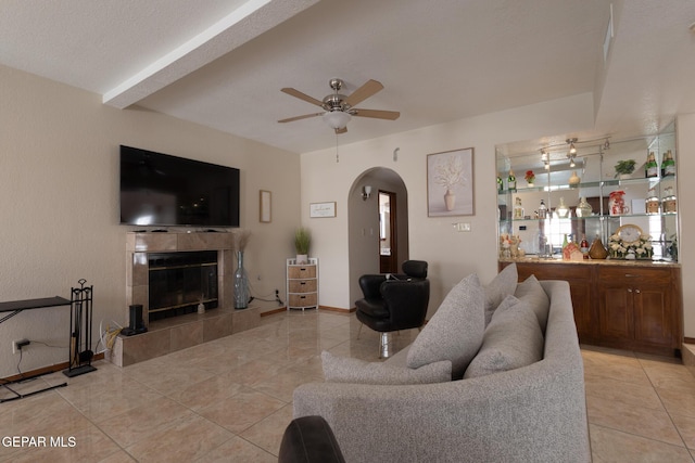 living room with a ceiling fan, light tile patterned floors, arched walkways, and a tiled fireplace