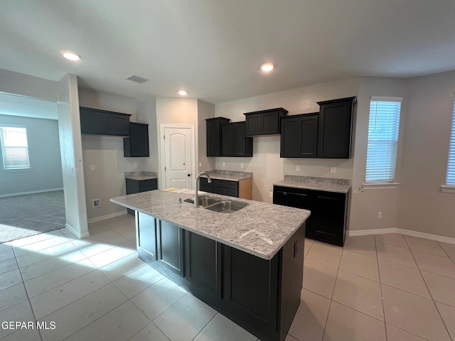 kitchen featuring visible vents, a kitchen island with sink, a sink, dark cabinetry, and baseboards