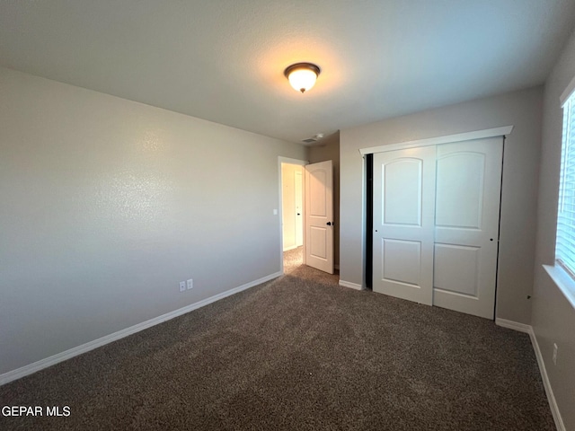 unfurnished bedroom with a closet, dark carpet, and baseboards