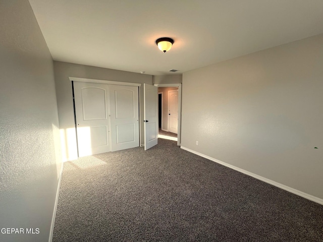 unfurnished bedroom featuring dark colored carpet, a closet, and baseboards