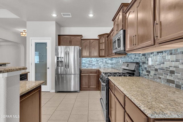 kitchen with visible vents, light stone counters, stainless steel appliances, backsplash, and light tile patterned flooring