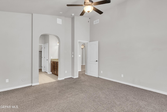 unfurnished bedroom featuring visible vents, arched walkways, baseboards, light colored carpet, and a high ceiling