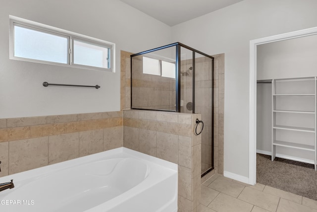 full bath with a walk in closet, a garden tub, a stall shower, tile patterned flooring, and baseboards