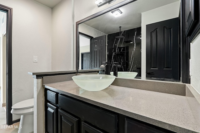 bathroom with toilet, a textured wall, a shower stall, and vanity