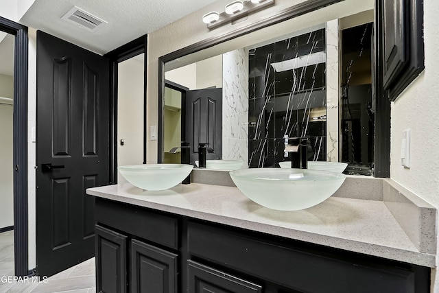 bathroom with a textured ceiling, double vanity, a sink, and visible vents