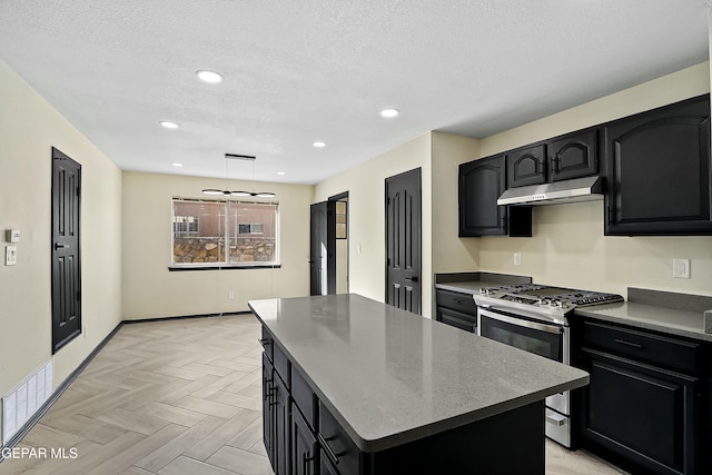 kitchen with dark cabinets, stainless steel range with gas stovetop, a kitchen island, and under cabinet range hood