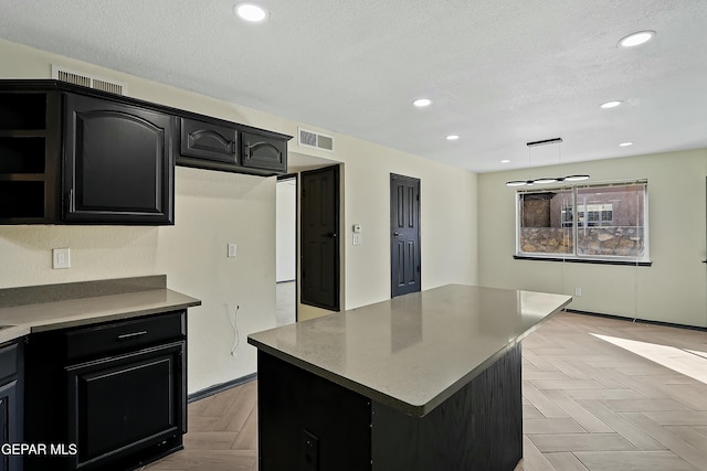 kitchen featuring a textured ceiling, dark cabinetry, decorative light fixtures, and a center island