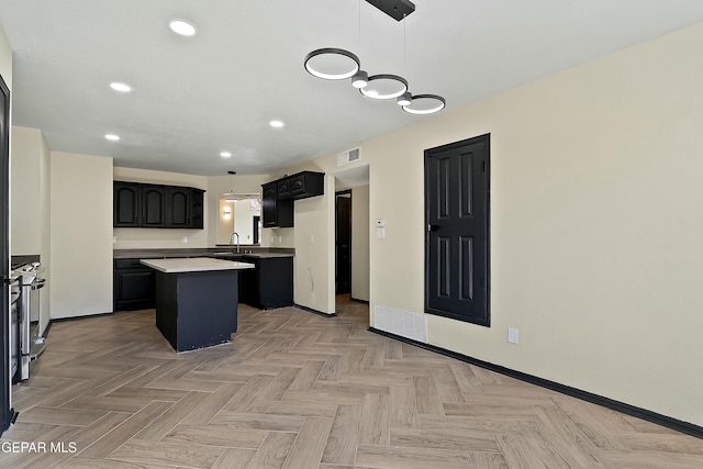 kitchen featuring a sink, visible vents, light countertops, hanging light fixtures, and a center island