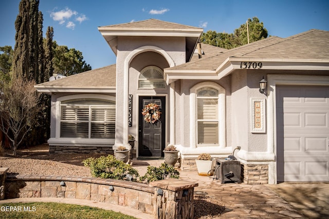 entrance to property with a garage, roof with shingles, and stucco siding