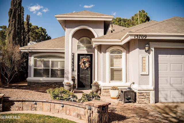 view of exterior entry featuring a garage, roof with shingles, and stucco siding