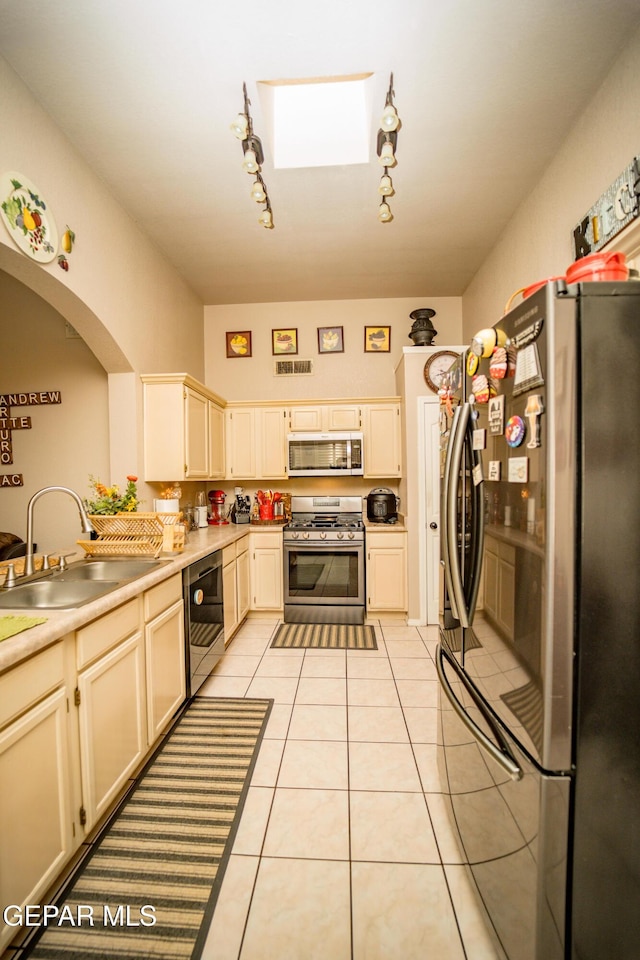 kitchen with light tile patterned floors, stainless steel appliances, a skylight, a sink, and light countertops