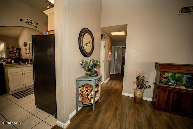 hallway with light wood-style floors, arched walkways, visible vents, and baseboards