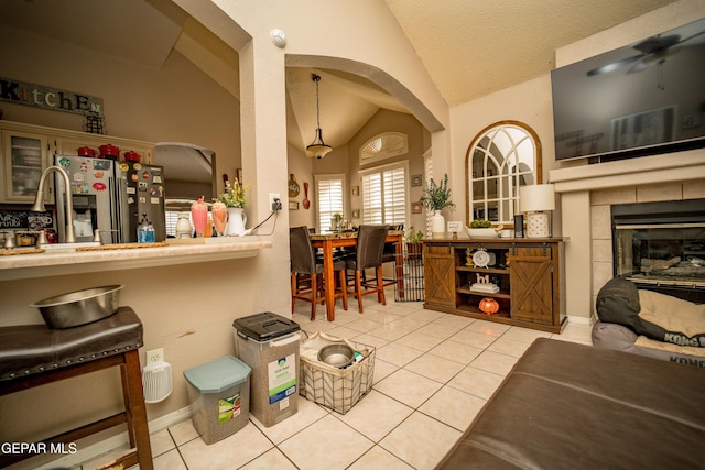 interior space featuring lofted ceiling, light tile patterned flooring, a tiled fireplace, and stainless steel fridge with ice dispenser