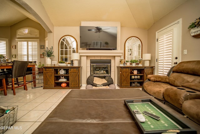 living room featuring vaulted ceiling, light tile patterned floors, a fireplace, and a ceiling fan