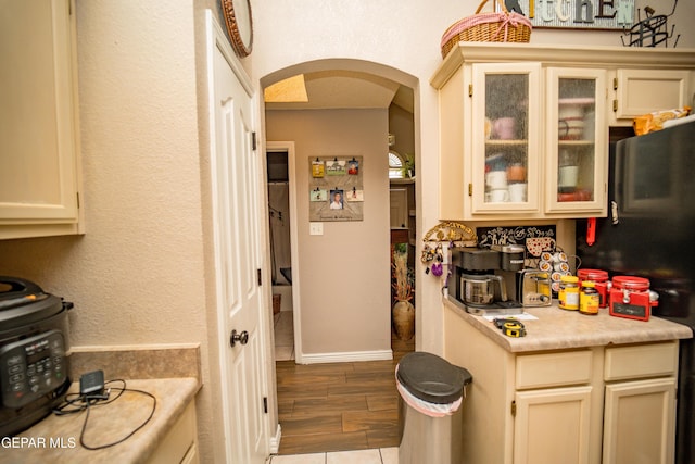 kitchen with arched walkways, wood finish floors, baseboards, light countertops, and glass insert cabinets