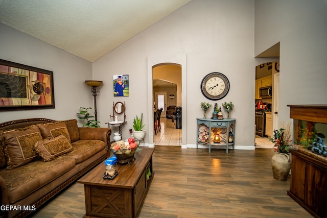 living area with arched walkways, a textured ceiling, wood finished floors, high vaulted ceiling, and baseboards