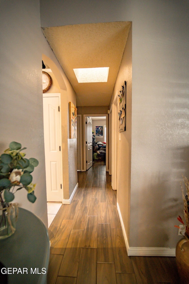 hallway with a skylight, dark wood finished floors, and baseboards