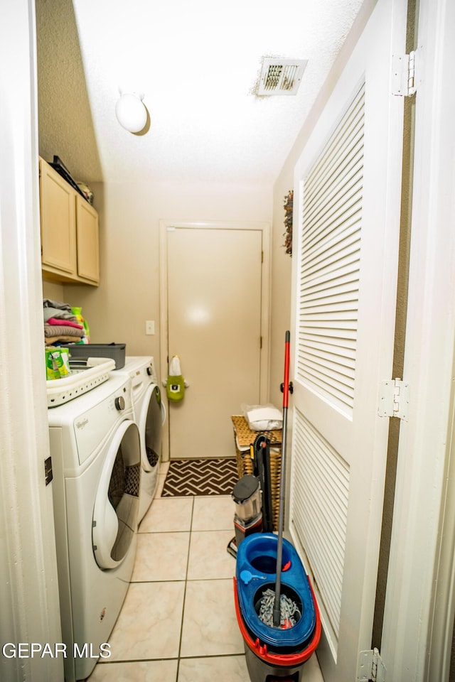 clothes washing area with washing machine and dryer, cabinet space, visible vents, and light tile patterned flooring