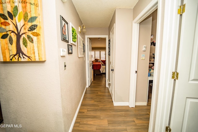 corridor featuring baseboards, dark wood finished floors, a textured ceiling, and a textured wall