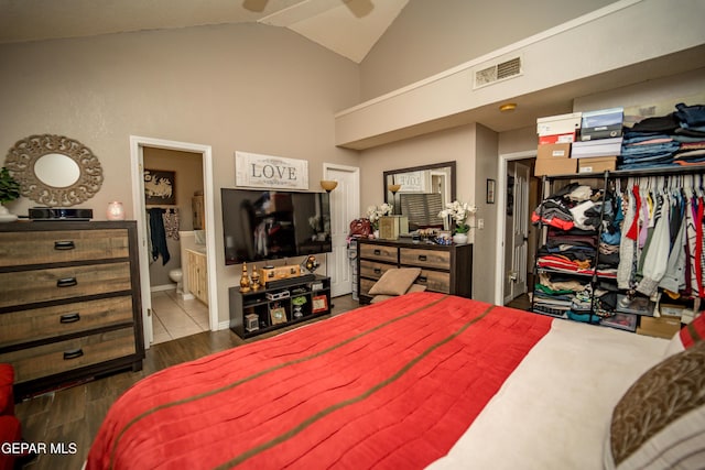 bedroom with connected bathroom, dark wood finished floors, visible vents, and vaulted ceiling