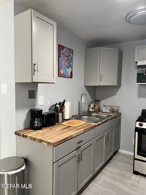 kitchen with a sink, wood counters, gray cabinets, light wood finished floors, and gas stove