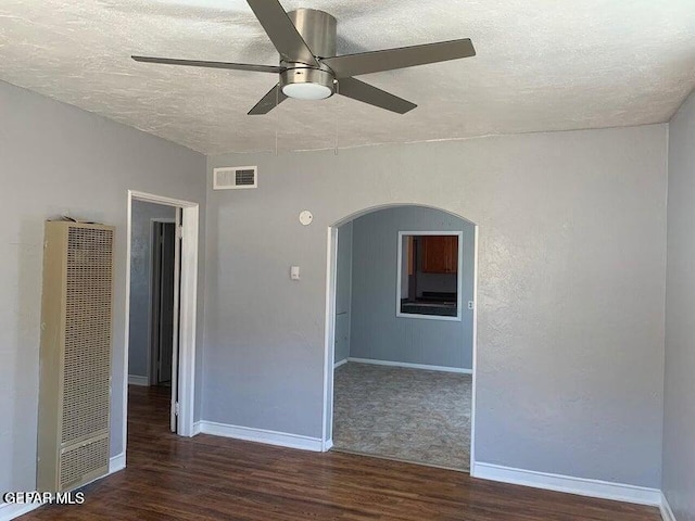 spare room featuring dark wood-style floors, arched walkways, visible vents, a heating unit, and a textured ceiling