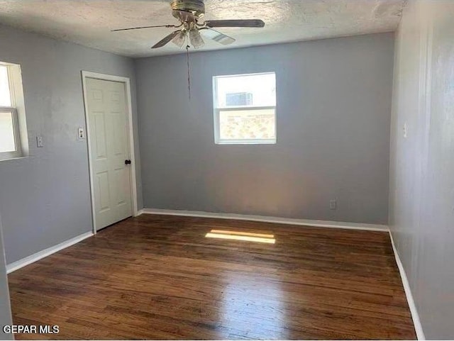 empty room featuring a textured ceiling, ceiling fan, dark wood-style flooring, and baseboards