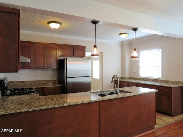 kitchen featuring light stone counters, decorative light fixtures, freestanding refrigerator, under cabinet range hood, and a sink