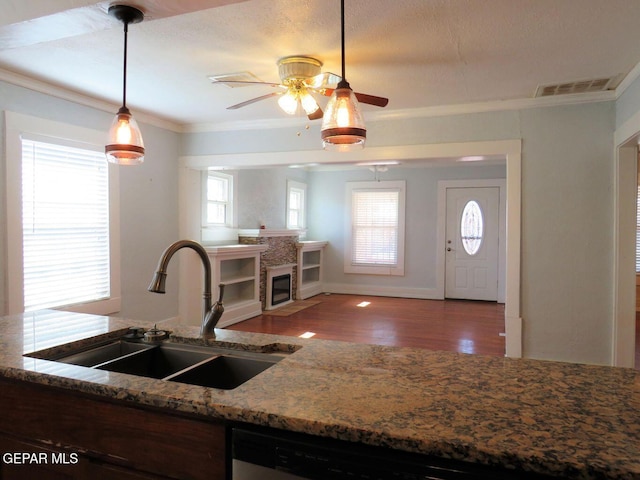 kitchen with wood finished floors, a sink, visible vents, decorative light fixtures, and crown molding