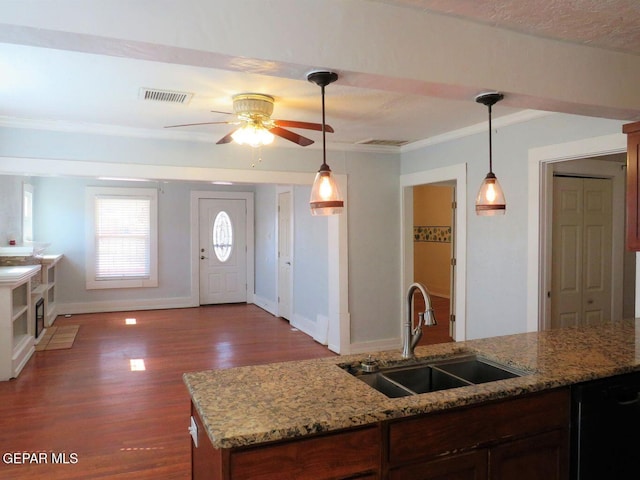 kitchen with light stone countertops, a sink, visible vents, and decorative light fixtures