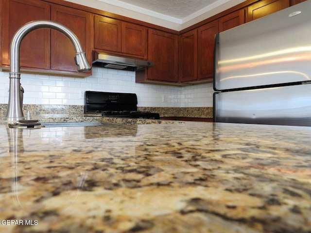 kitchen featuring tasteful backsplash, ornamental molding, freestanding refrigerator, black range oven, and under cabinet range hood