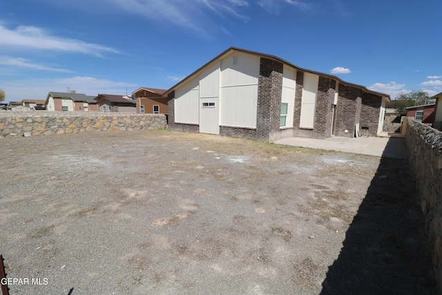 view of side of property with a residential view, a patio area, brick siding, and fence