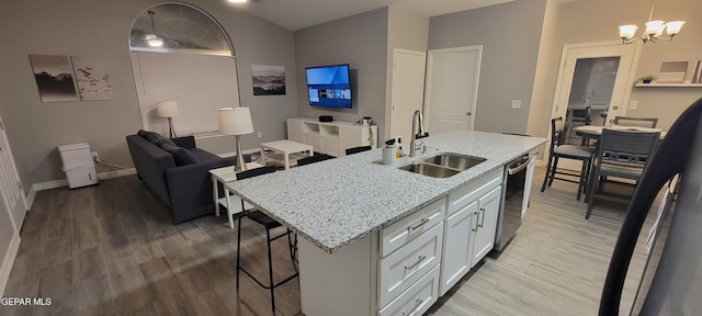 kitchen featuring a center island with sink, light stone countertops, white cabinetry, pendant lighting, and a sink