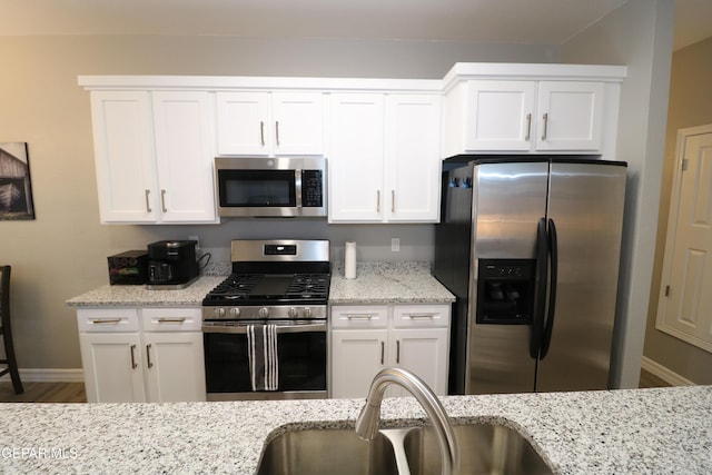 kitchen with white cabinets, appliances with stainless steel finishes, light stone counters, and a sink