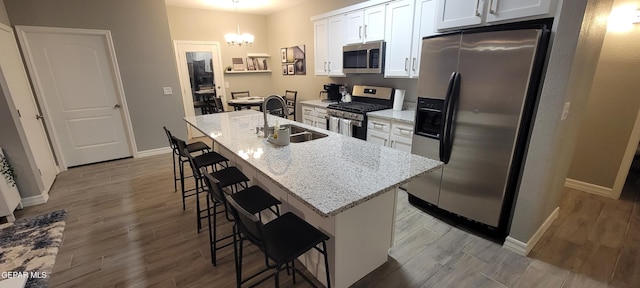 kitchen with an island with sink, appliances with stainless steel finishes, a kitchen breakfast bar, white cabinetry, and a sink