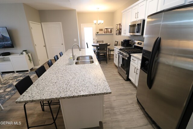 kitchen with appliances with stainless steel finishes, white cabinetry, an island with sink, and a kitchen bar