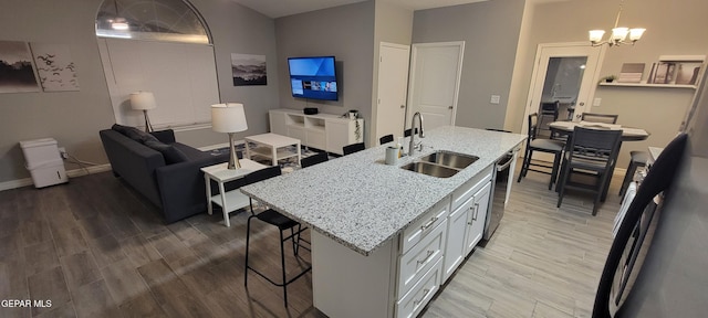 kitchen featuring light stone counters, a sink, white cabinets, a center island with sink, and decorative light fixtures