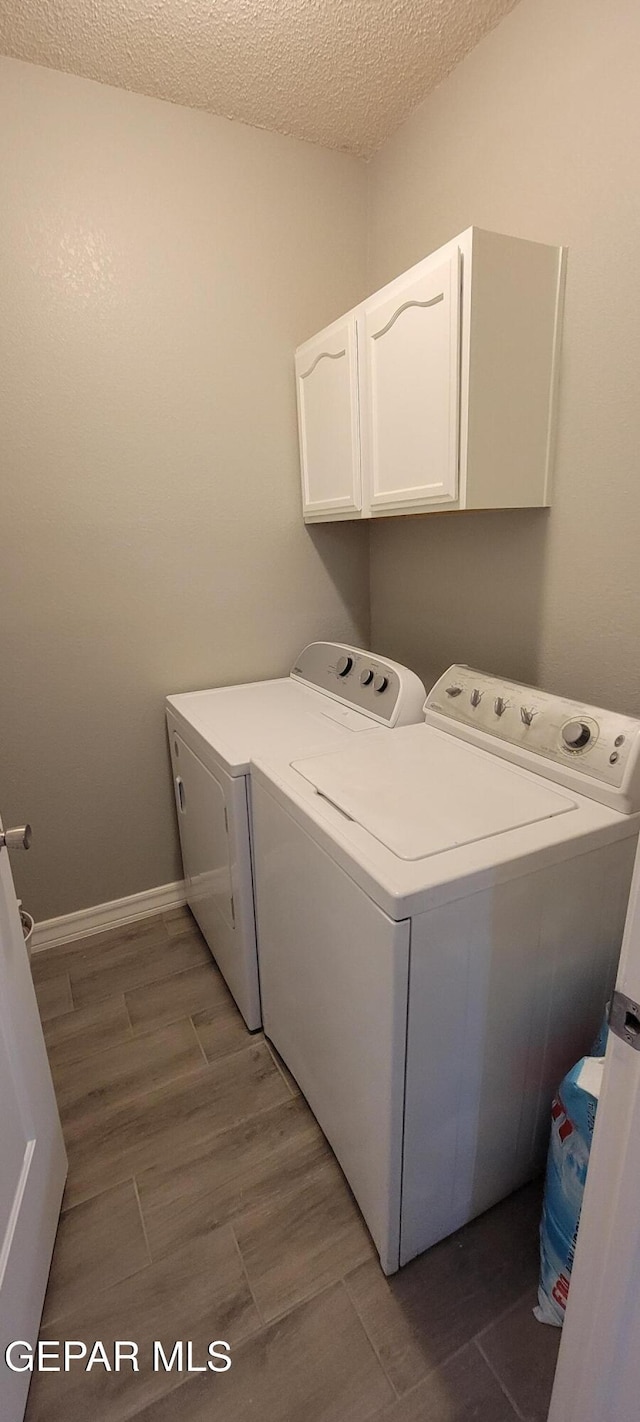 clothes washing area featuring a textured ceiling, washing machine and dryer, baseboards, cabinet space, and dark wood-style floors