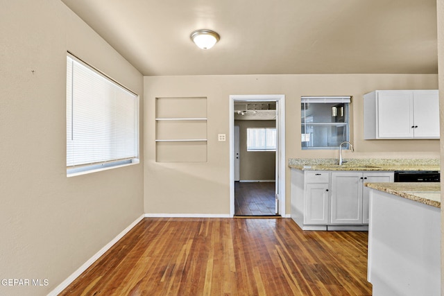 kitchen with dark wood finished floors, white cabinetry, a sink, light stone countertops, and baseboards