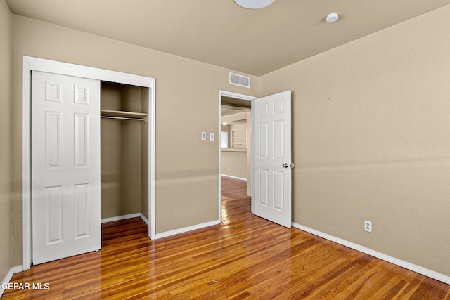 unfurnished bedroom featuring a closet, visible vents, baseboards, and wood finished floors