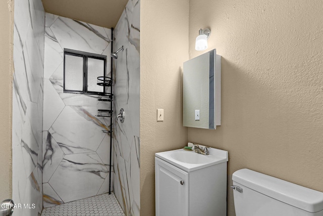 bathroom featuring toilet, a textured wall, a marble finish shower, and vanity