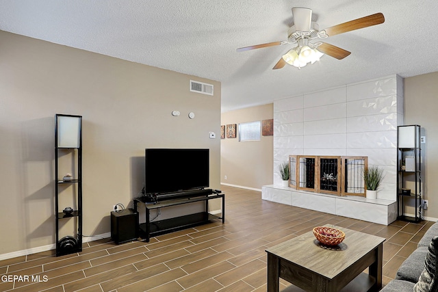 living room with visible vents, a tiled fireplace, wood tiled floor, a textured ceiling, and baseboards