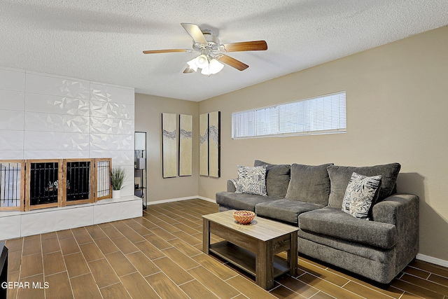 living area featuring baseboards, a tile fireplace, ceiling fan, a textured ceiling, and wood finish floors