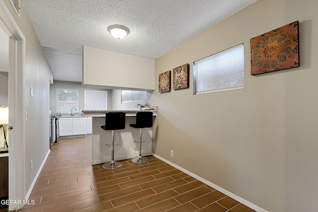 kitchen with a breakfast bar area, light countertops, wood tiled floor, white cabinetry, and baseboards