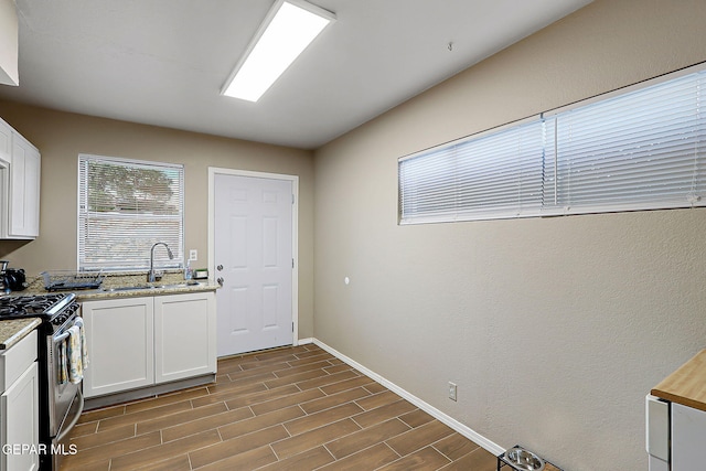 kitchen featuring a sink, white cabinets, stainless steel range with gas stovetop, and wood finish floors