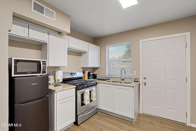 kitchen with visible vents, white cabinets, light stone counters, appliances with stainless steel finishes, and a sink